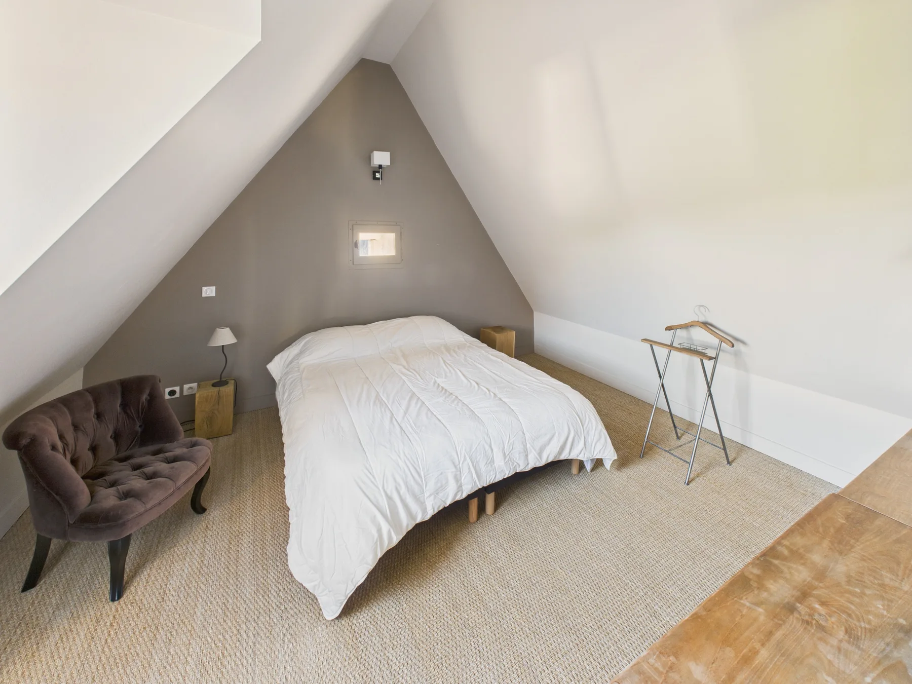 A bedroom with a bed beneath a sloped ceiling and a small armchair.