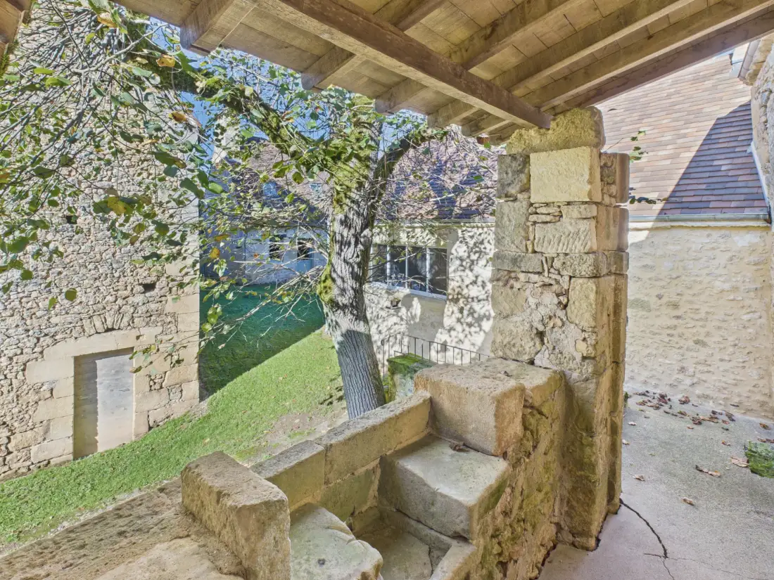 Stone terrace with steps overlooks a leafy courtyard and neighboring stone buildings.