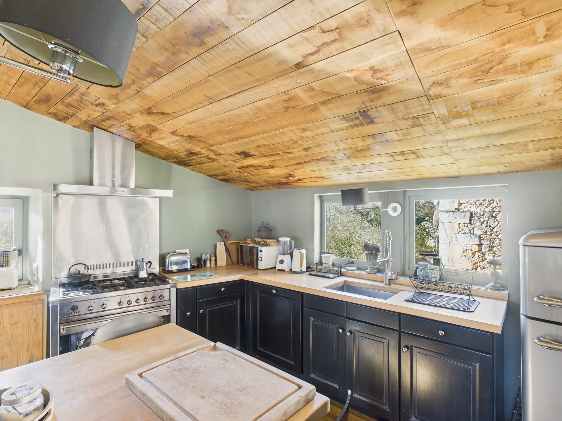 A kitchen with dark cabinetry, a large range, and windows above the counter.