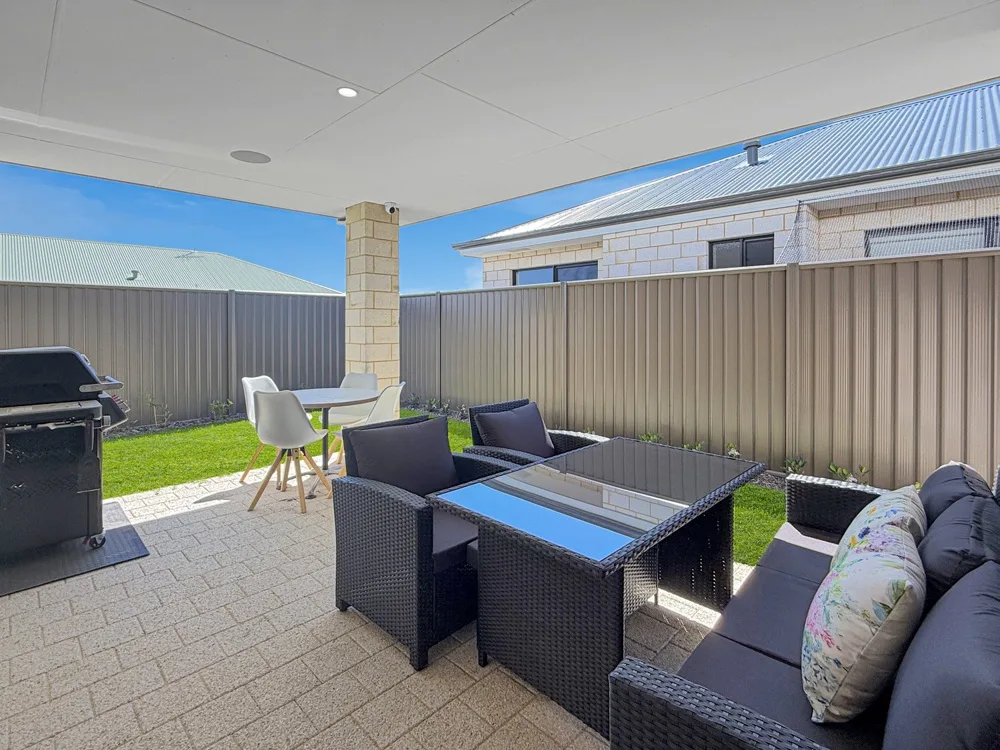 Patio exterior con comedor y asientos al aire libre junto a una pequeña zona de césped.
