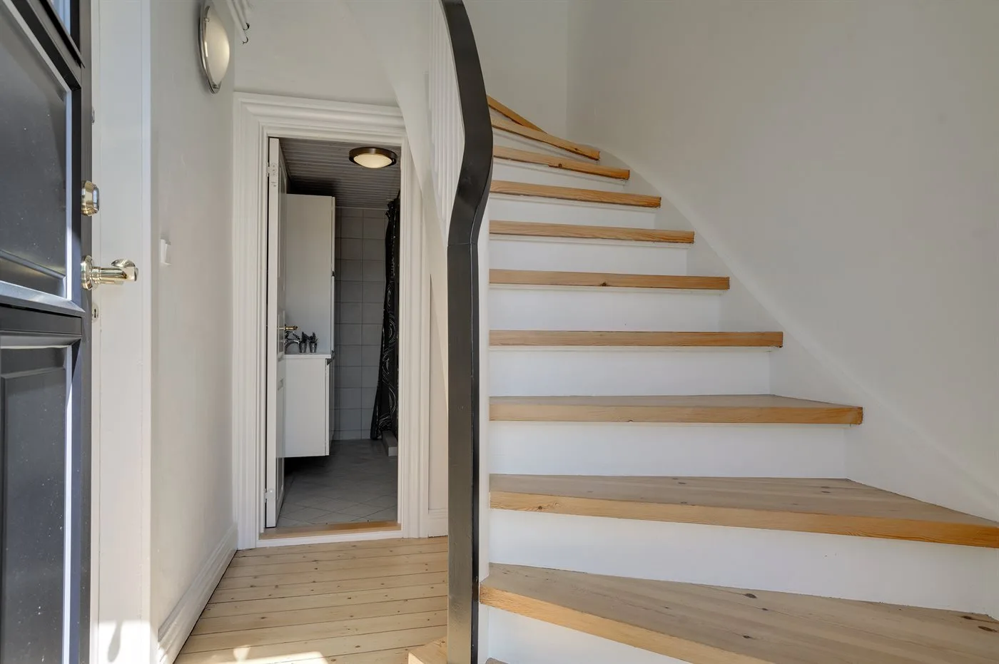 Una escalera con peldaños de madera sube junto a una puerta abierta.