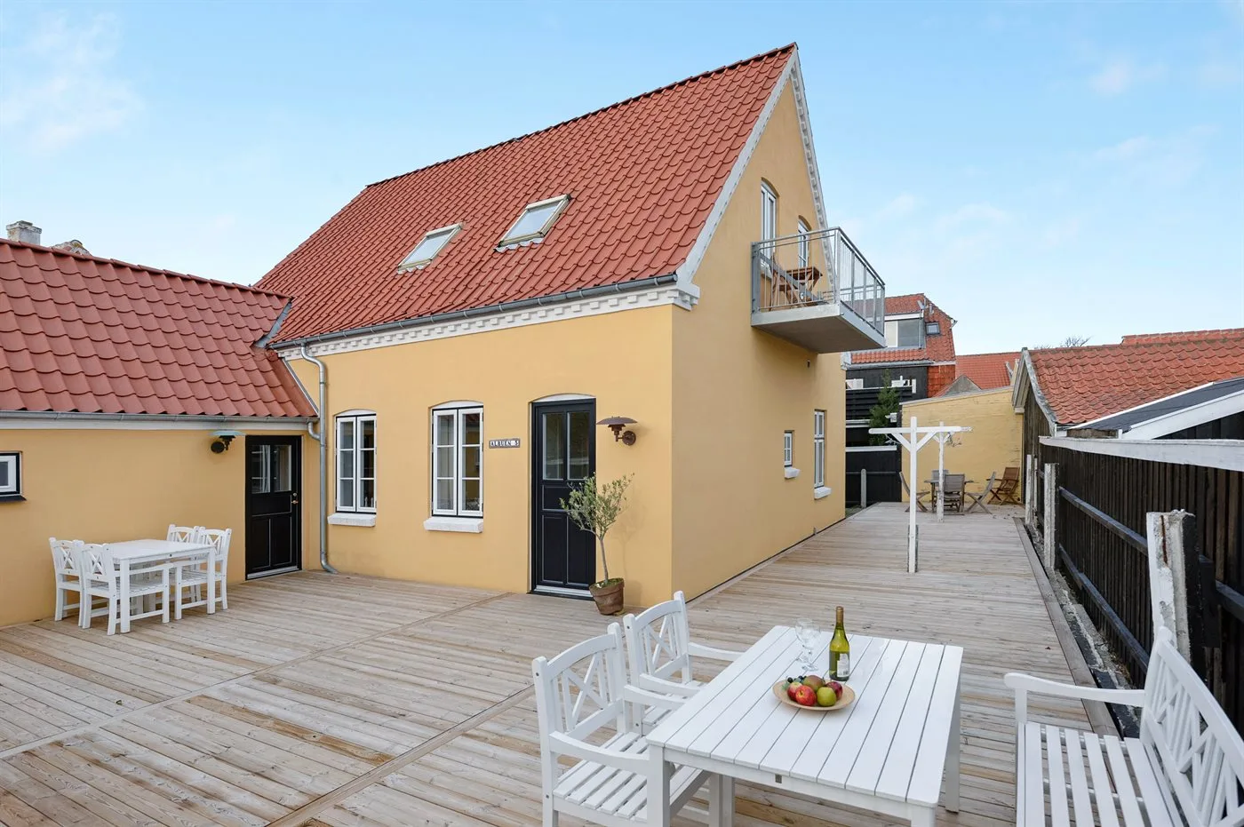 Una casa amarilla da a una amplia terraza de madera con asientos al aire libre.