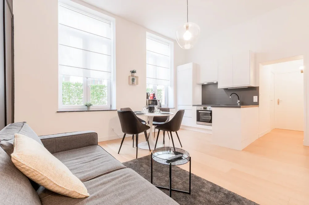 A bright open-plan living area with a sofa, dining table, and kitchen.
