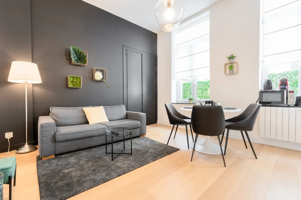 Living room and dining area with a gray sofa, dining table, and large windows.