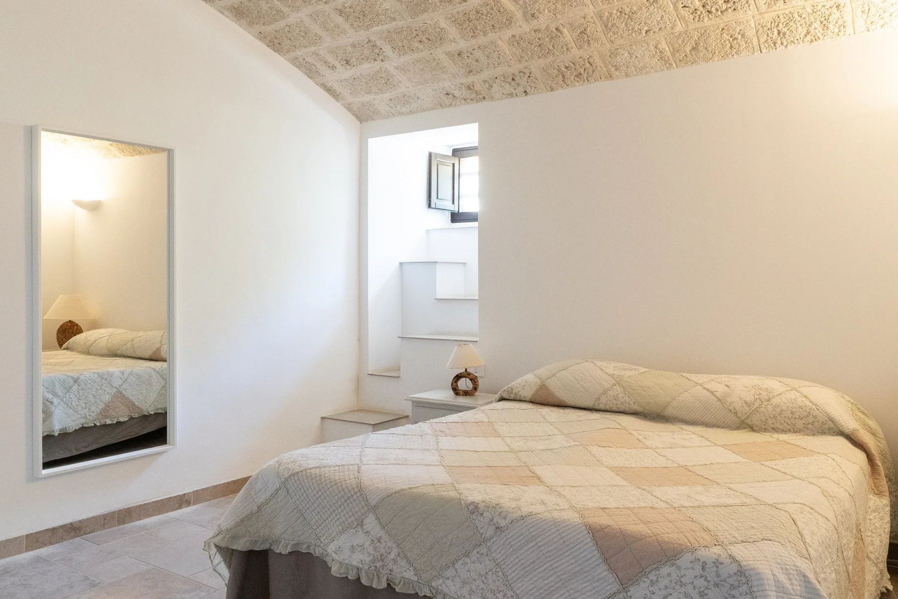 A bedroom with a bed covered in a light patterned quilt.