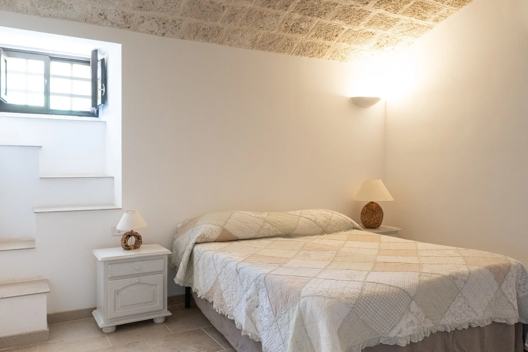 A bedroom with a bed, bedside tables, and a small window.