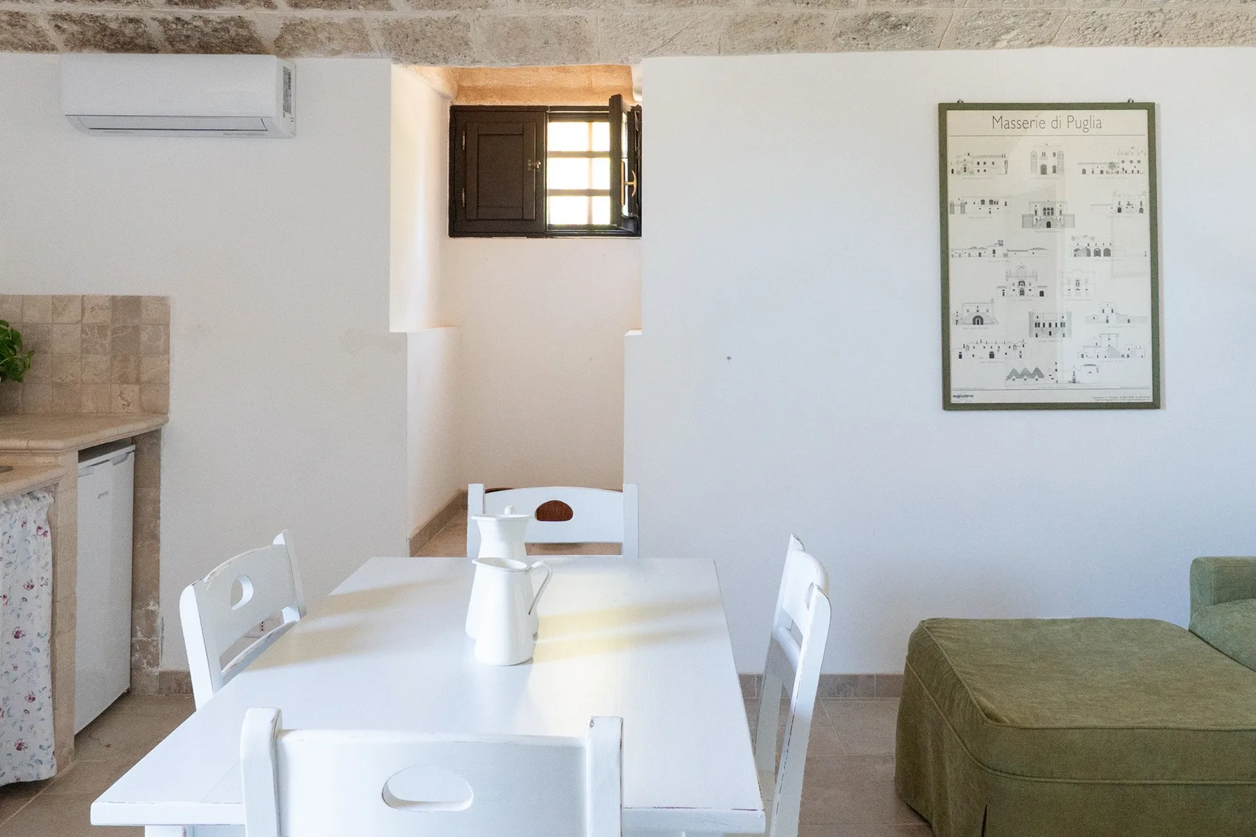 A bright dining area with a white table and seating beside a green upholstered couch.