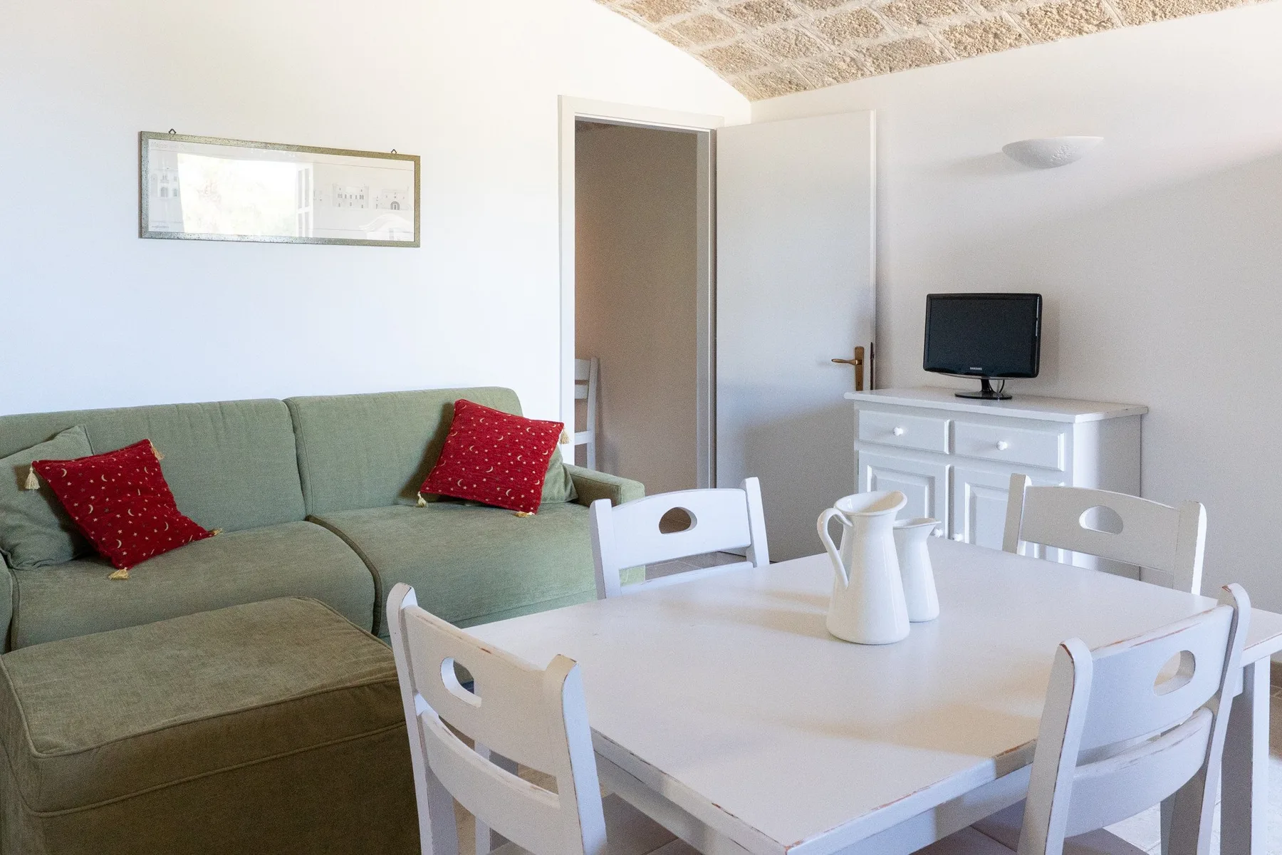 A dining area with a white table and seating beside a green sofa.