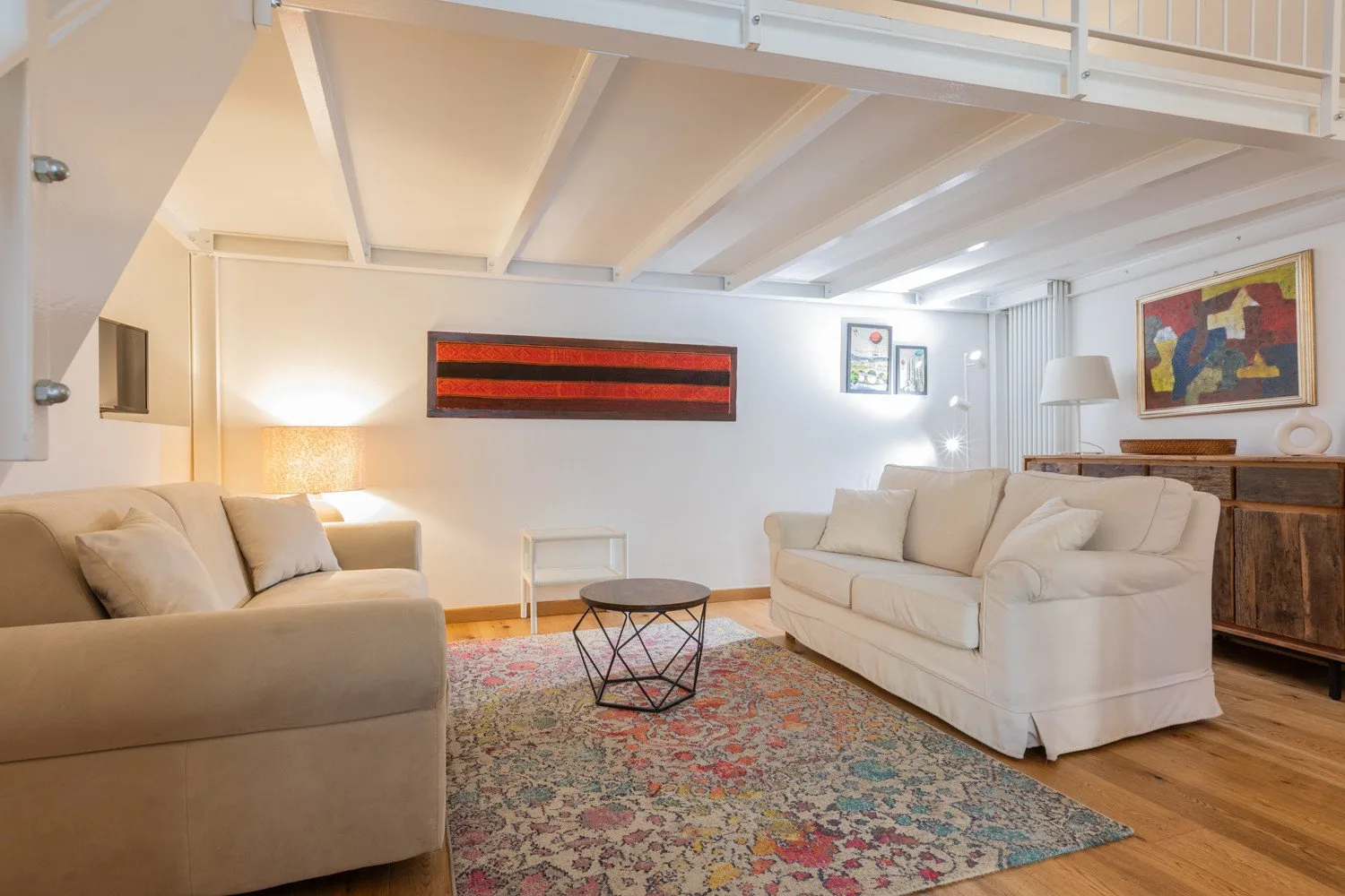 A bright living room with light-colored seating arranged around a patterned rug.