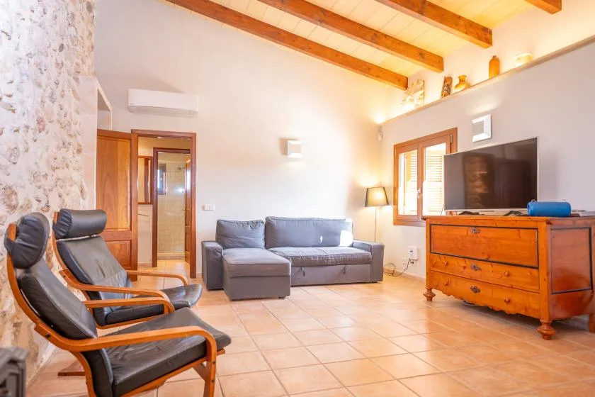 A living room with seating, a television, and exposed wooden ceiling beams.