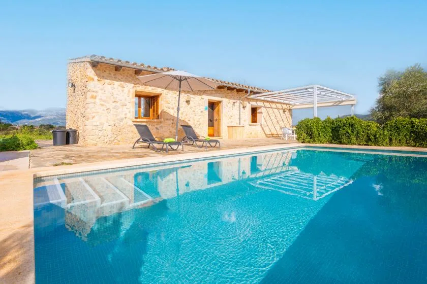 A swimming pool beside a stone house, with lounge seating on the patio.