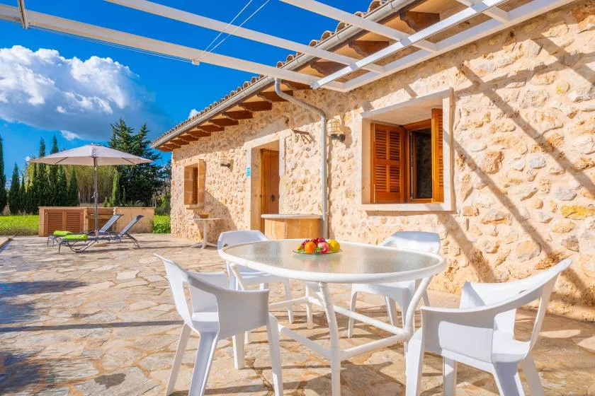 A stone house opens onto a sunny patio with outdoor dining furniture.
