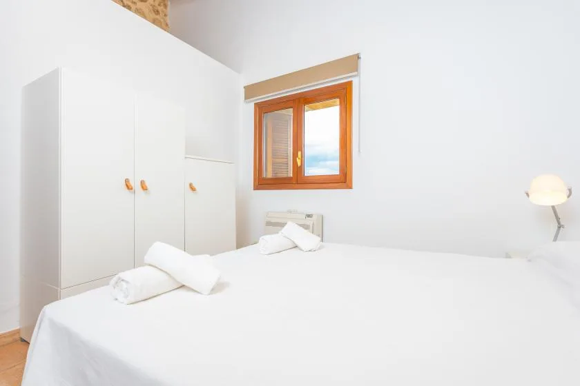 A bright bedroom with white bedding and a wooden-framed window.