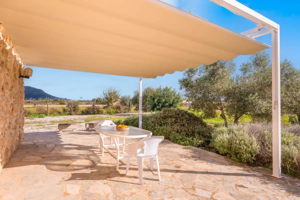 A shaded outdoor patio with a table and seating overlooks a garden.