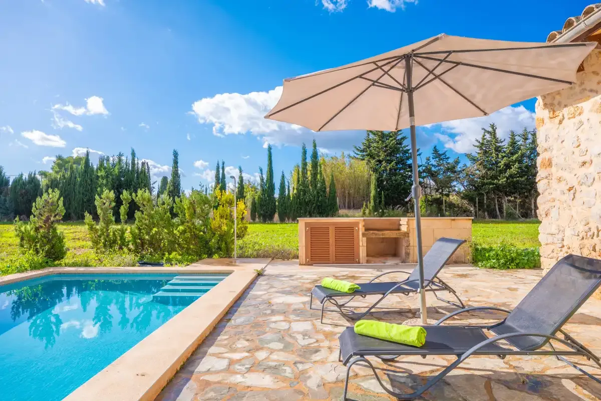 A swimming pool beside a stone patio with lounge seating and a large umbrella.