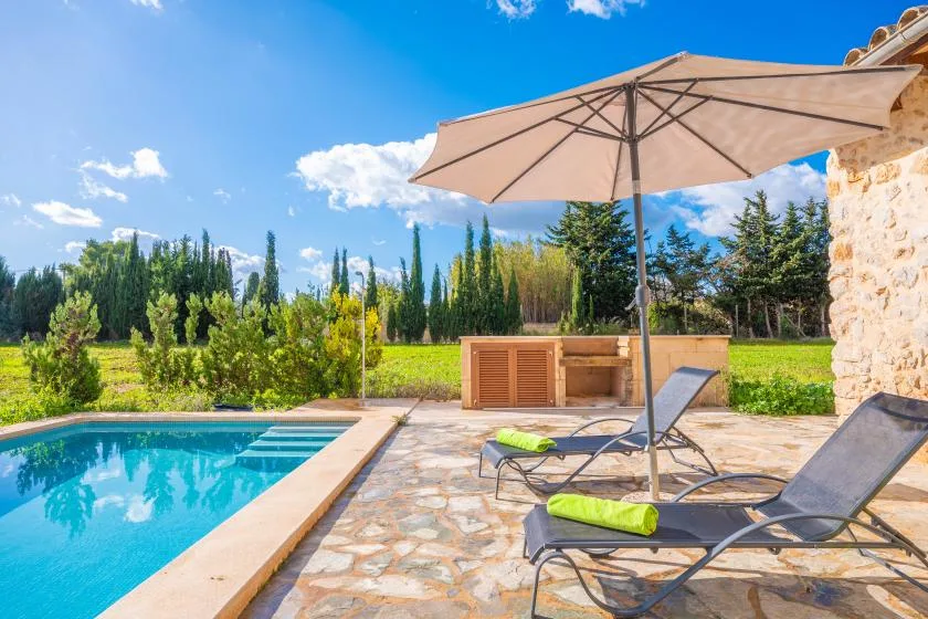 A swimming pool beside a stone-paved patio with loungers and an umbrella.
