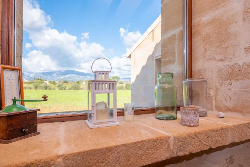 A stone windowsill holds glass jars and a lantern overlooking a green field.