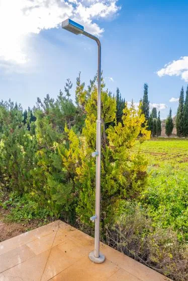 An outdoor shower stands beside green shrubs and an open grassy area.