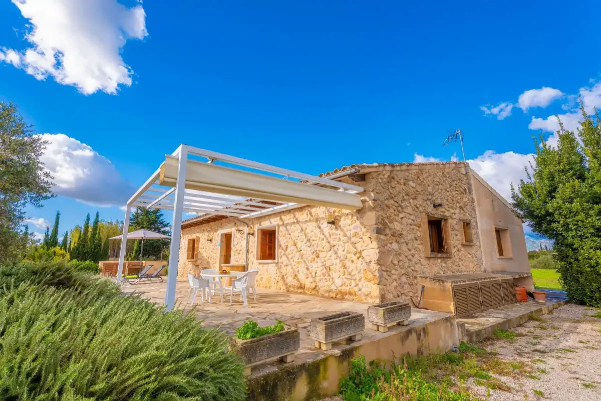 A stone house with a white pergola over an outdoor patio.
