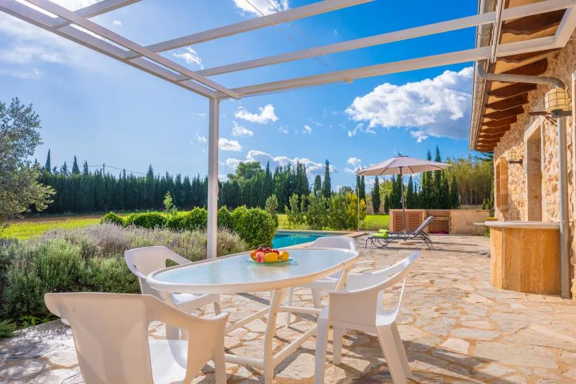 A sunny outdoor dining terrace overlooks a garden, with a pool and umbrella nearby.