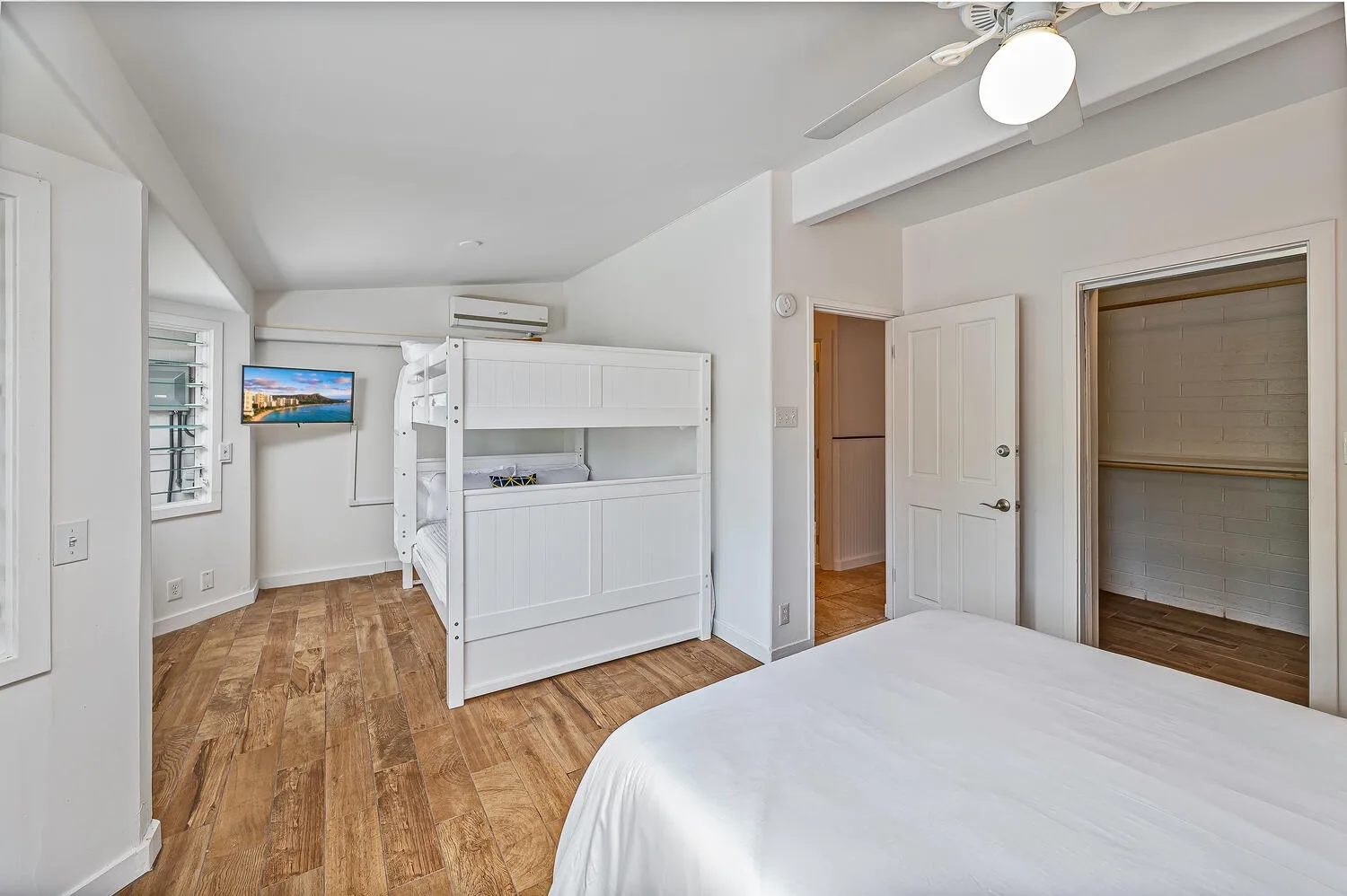 Un dormitorio luminoso con una cama, una litera blanca y suelo de madera.