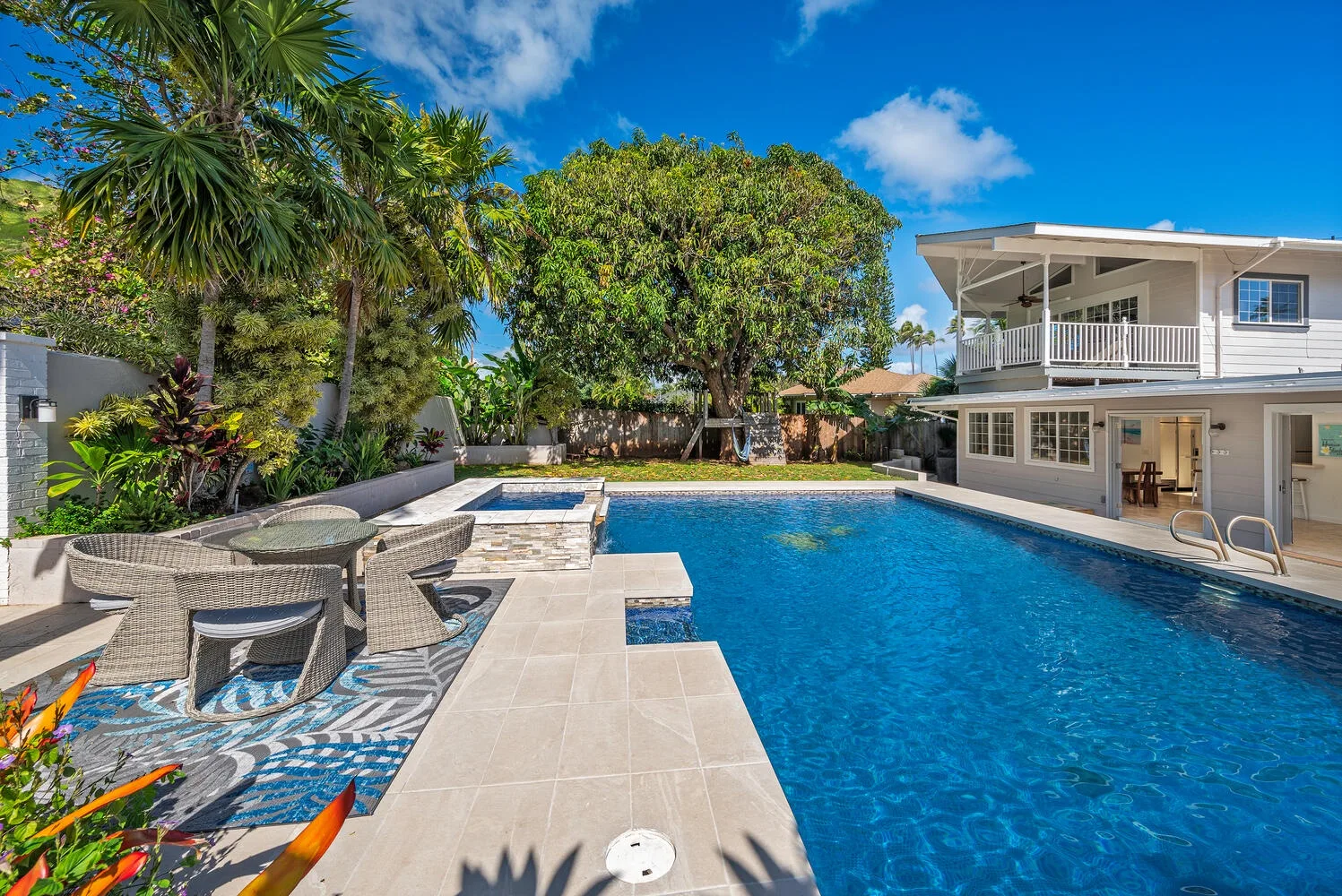 Una piscina al aire libre junto a un patio con asientos y una casa blanca.
