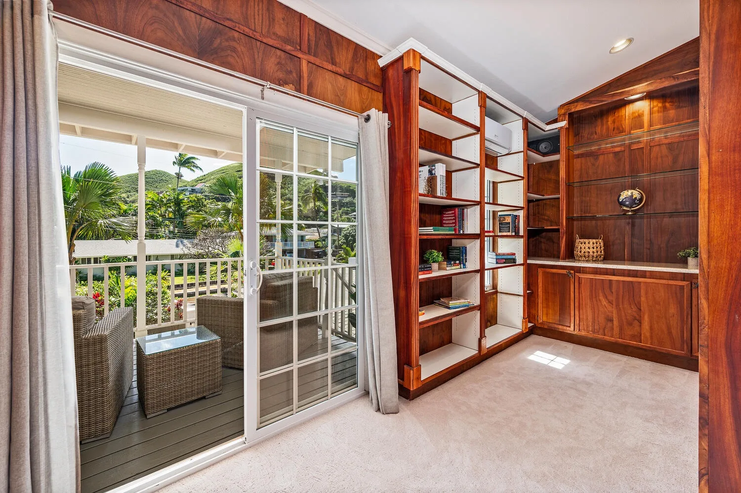 Una habitación con estantes y gabinetes de madera junto a puertas corredizas de vidrio que dan a un balcón.