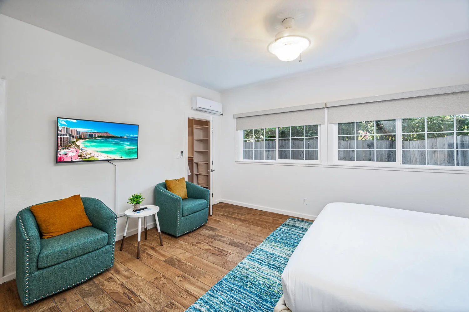 Un dormitorio luminoso con una cama, dos sillones y una ventana amplia.