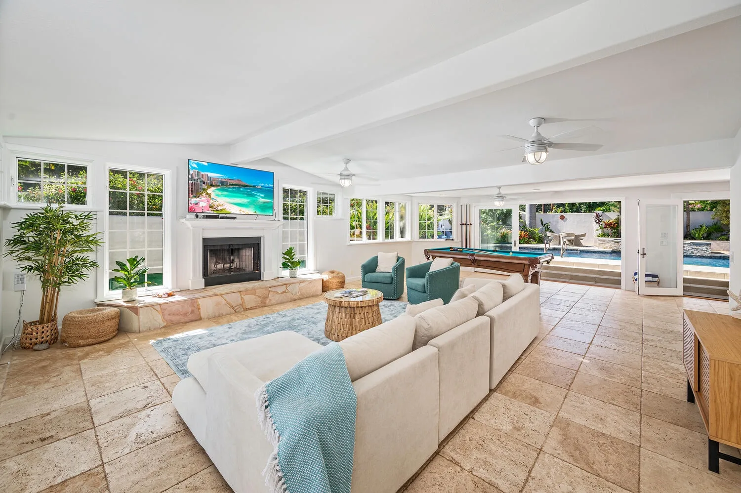 Una sala luminosa con asientos, una chimenea y una piscina visible a través de las ventanas.