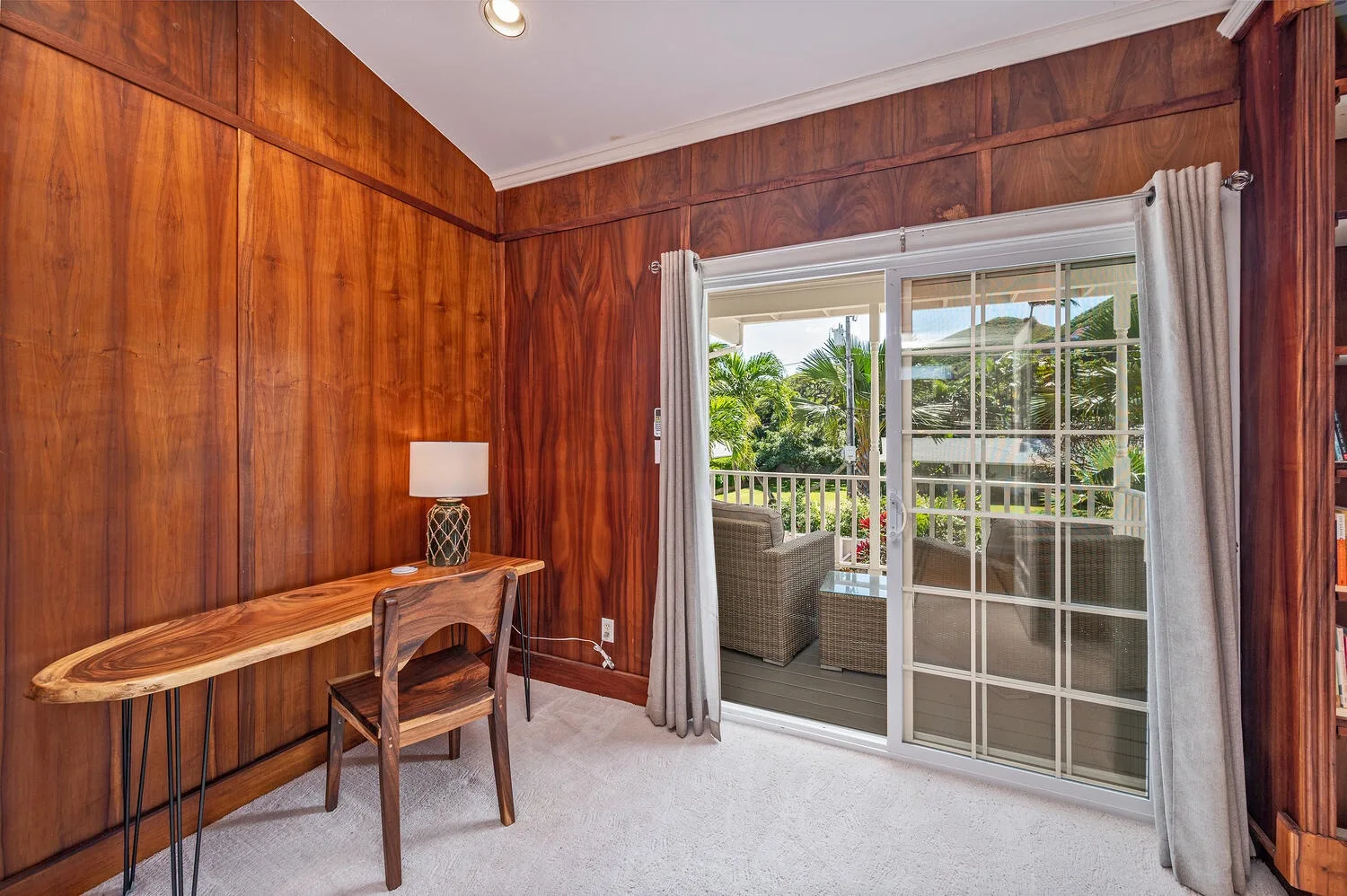 Una habitación revestida de madera, con un escritorio junto a puertas corredizas de vidrio que dan a un patio.