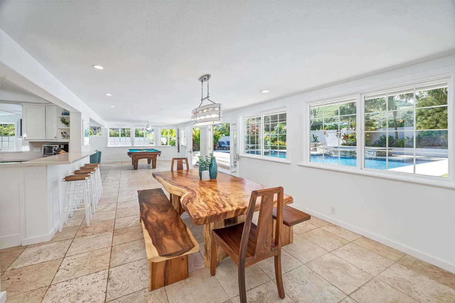 Un comedor luminoso tiene una mesa de madera junto a grandes ventanas con vistas a una piscina.