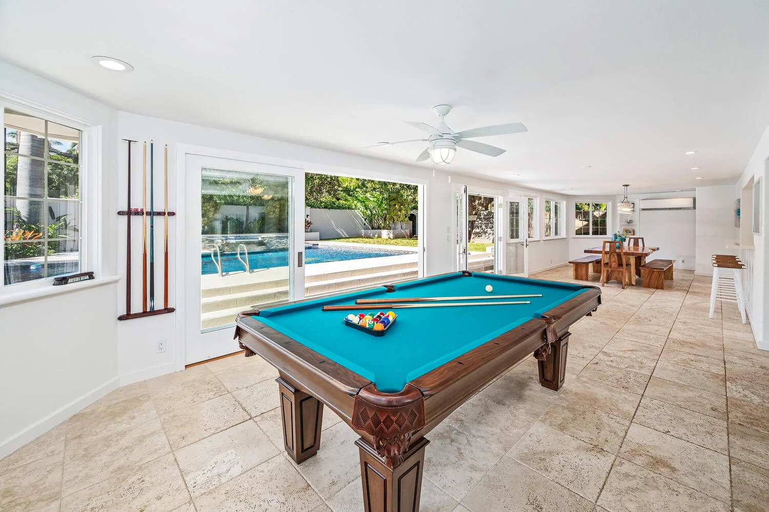 Una luminosa sala de juegos tiene una mesa de billar y una piscina visible afuera.
