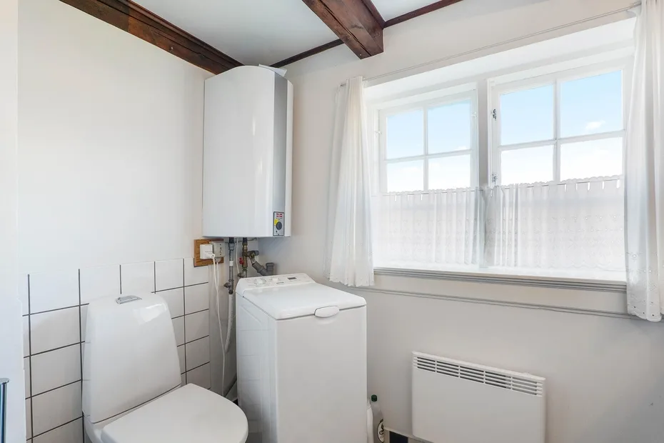 A laundry area with a washing machine beside a toilet and bright windows.