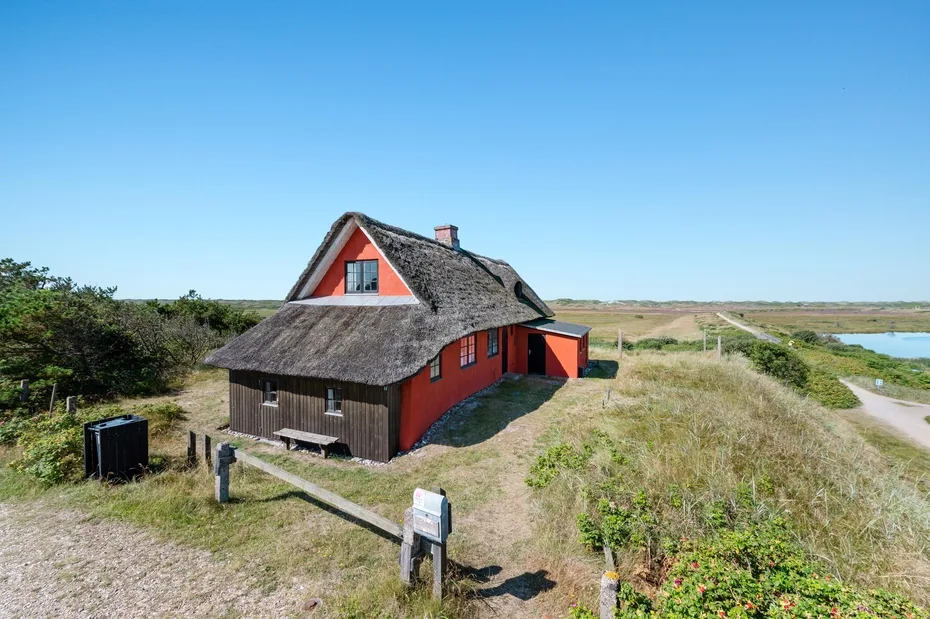 A red cottage with a thatched roof stands in open grassy surroundings.