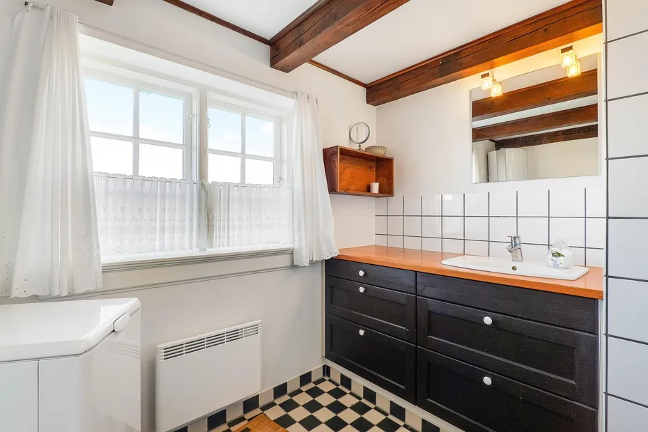 A bathroom vanity with a mirror sits beside a curtained window.