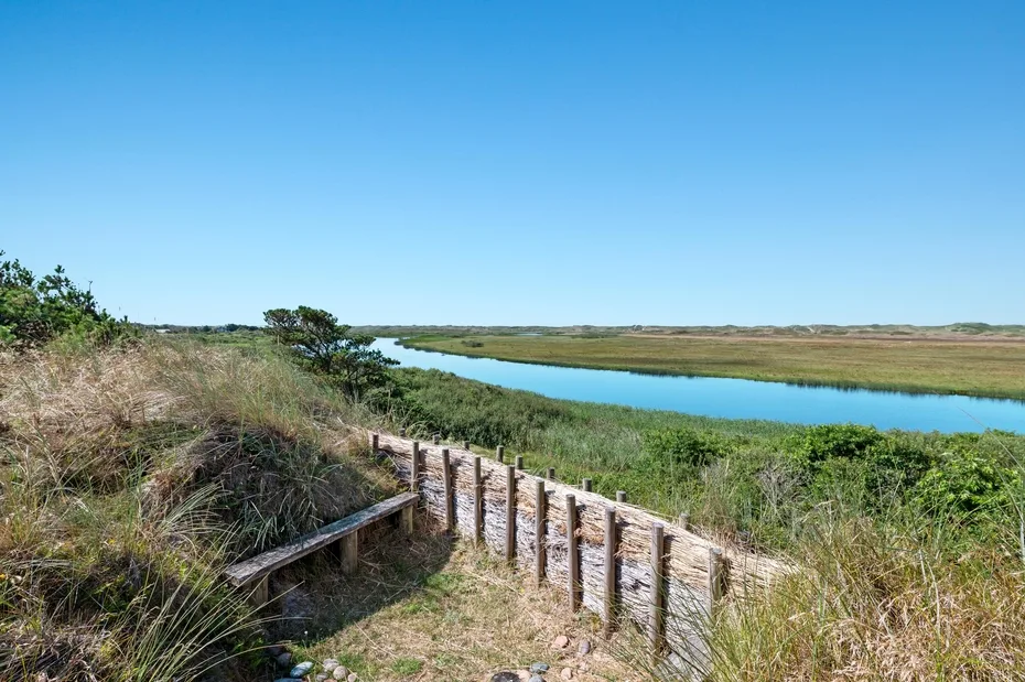 A wooden boardwalk crosses grassy marshland beside a winding waterway.