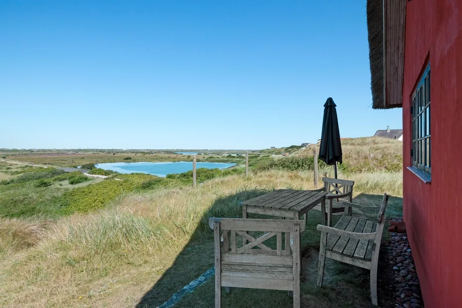 A wooden outdoor seating area overlooks a grassy landscape and water.
