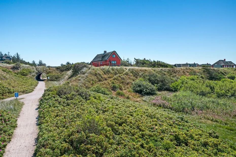 A red house stands on a grassy hillside beside a winding path.