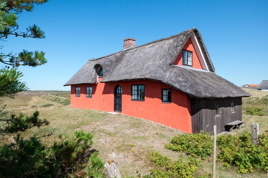 Thatched cottage in a grassy landscape under a clear blue sky.
