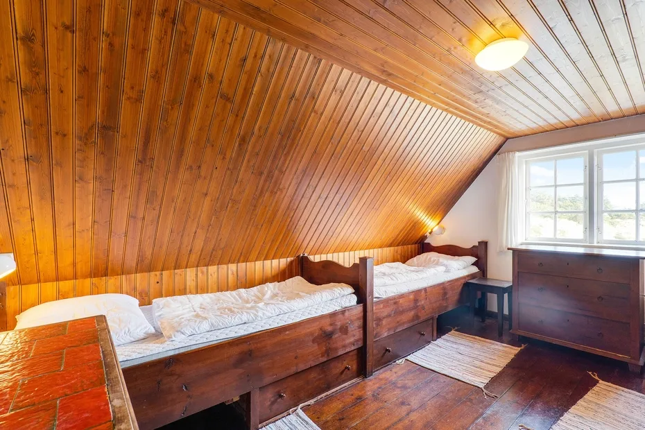 A wood-paneled bedroom with beds, a dresser, and a bright window.