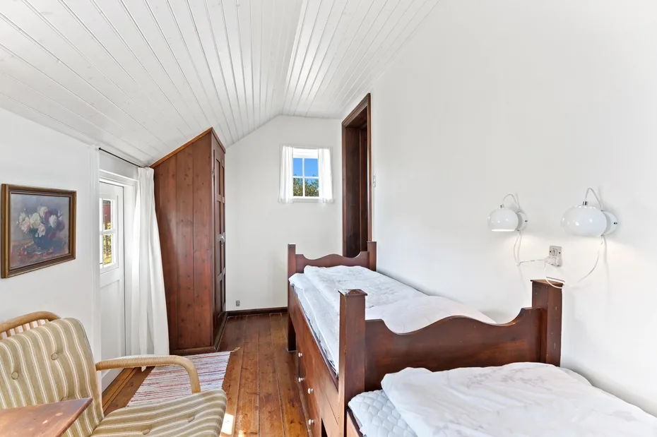 A bright bedroom with wooden beds, a striped armchair, and a small window.