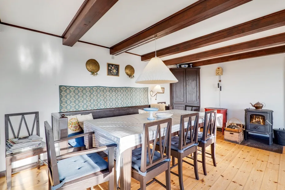 A dining room with a long table and wooden chairs beneath exposed ceiling beams.