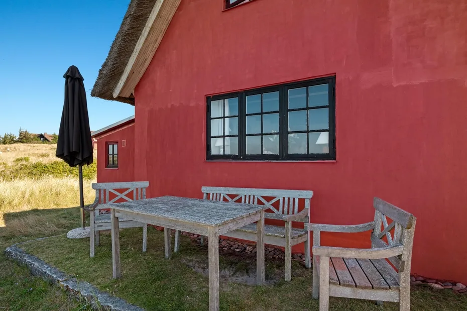 Outdoor seating beside a red building, with a table and closed umbrella.