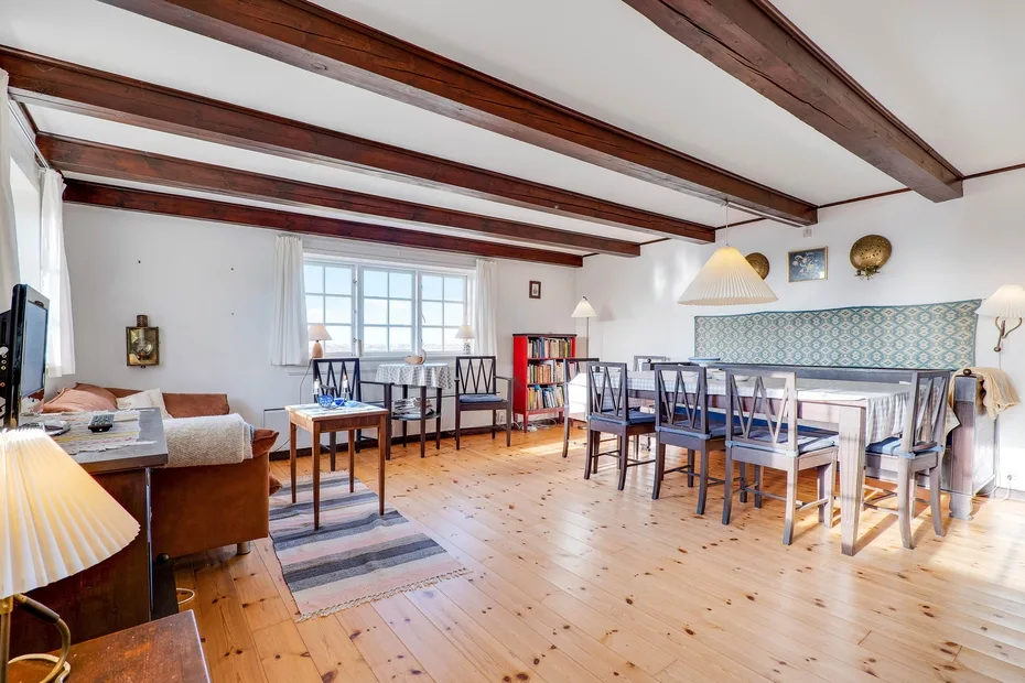 A bright dining and living room with exposed ceiling beams and a long dining table.