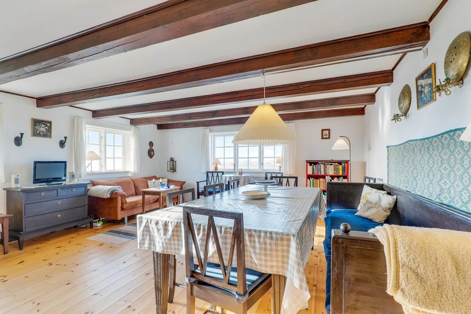 A bright dining and living room with a long table beneath exposed wooden beams.