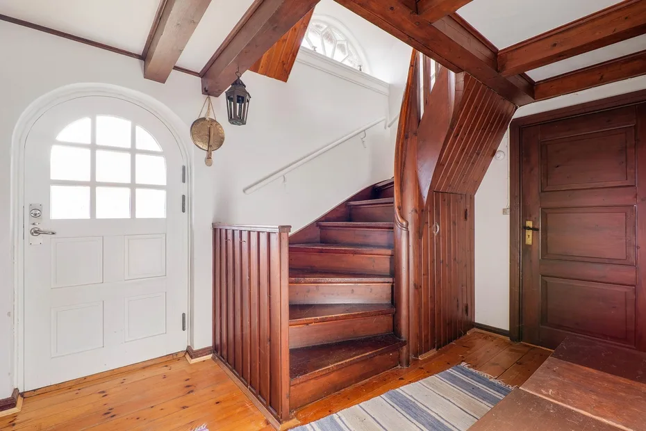 An interior entryway with a wooden staircase and white door.