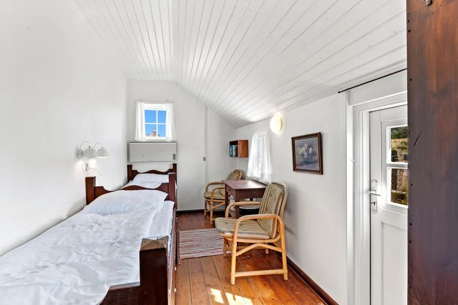 A bright bedroom with two beds, wicker seating, and a wooden floor.