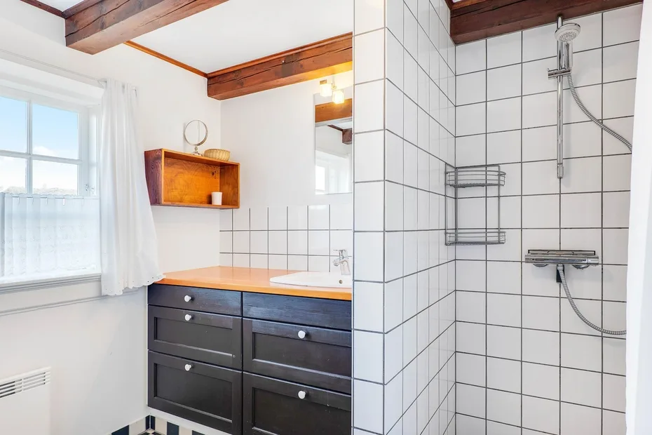 A bright bathroom with a dark vanity and a tiled shower.