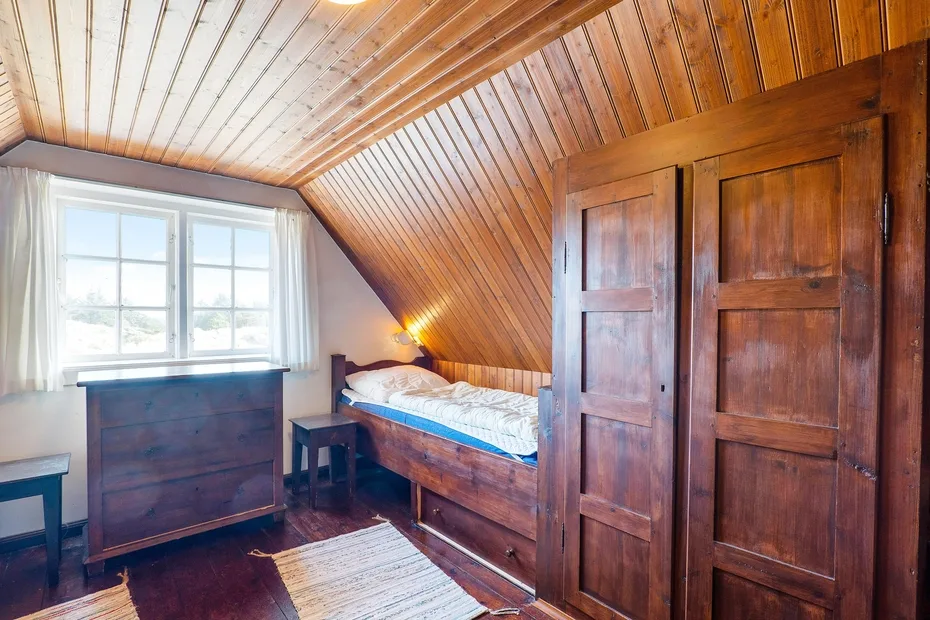 A wood-paneled bedroom with a bed beside a bright window.