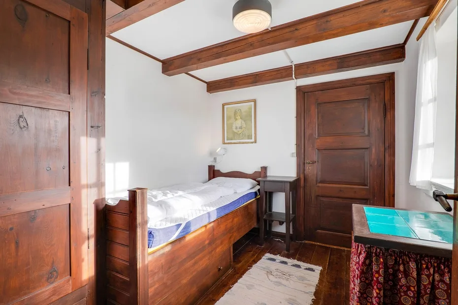 A bedroom with a wooden bed, exposed ceiling beams, and a small table.